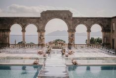 an outdoor wedding setup with clear chairs and flowers on the water's edge in front of arches