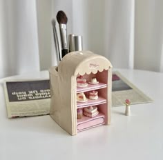 a small doll house with makeup brushes and other items in the holder, on a white table