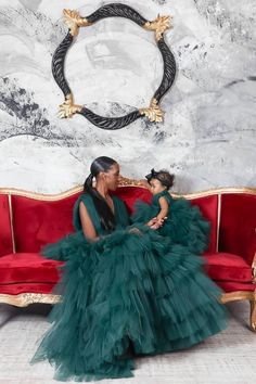 a mother and daughter sitting on a red couch in front of a wall with a circular mirror