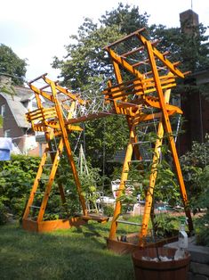 a wooden structure sitting on top of a lush green field next to a tree filled with lots of plants