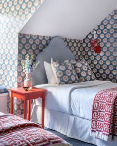 two beds in a room with blue and white wallpaper on the walls, one has a red end table next to it