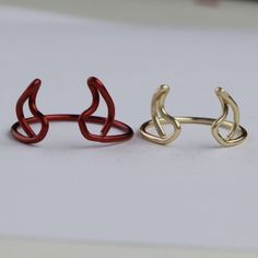 two gold and red rings sitting next to each other on a white surface with one ring in the shape of an animal's head