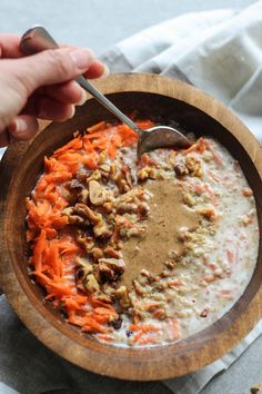 a person holding a spoon in a bowl of carrots and oatmeal