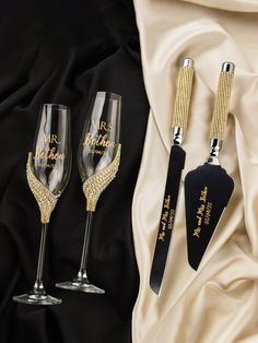 two wine glasses with black and gold handles are next to a pair of knifes