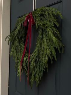 a wreath hanging on the front door of a house with a red ribbon tied around it