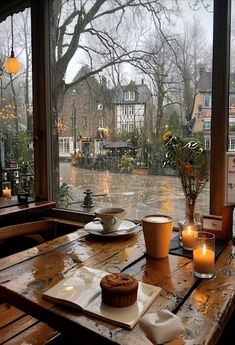 a wooden table topped with a cupcake next to a window covered in raindrops