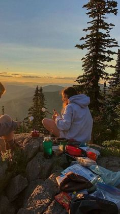 two people sitting on top of a mountain next to each other with food and drinks