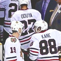 the hockey players are talking to each other in front of an official man wearing a suit and tie