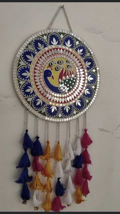 a decorative wall hanging with tassels on it's sides and an image of a peacock in the center