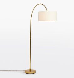 a gold floor lamp with a white shade on it's base and a round light bulb