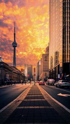 a city street with tall buildings in the background and a sky filled with orange clouds