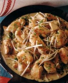 a skillet filled with chicken and cheese on top of a blue table cloth next to utensils