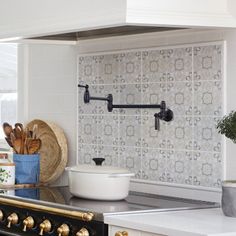 a stove top oven sitting inside of a kitchen next to a potted plant and wooden utensils