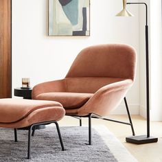 an orange chair and footstool in a living room with a painting on the wall