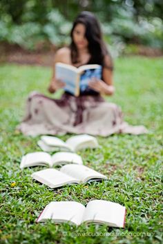 a woman sitting on the grass reading a book with an open book in front of her