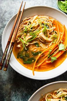 two bowls filled with noodles and vegetables next to chopsticks on a table top