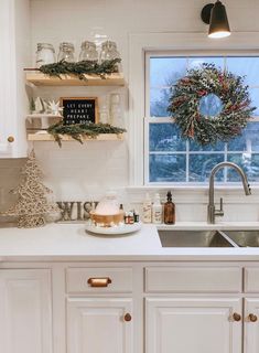 a kitchen with white cabinets and christmas wreath on the window sill above the sink