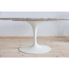 an oval dining table with marble top and white pedestal base, on wooden flooring