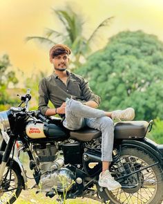 a man sitting on the back of a motorcycle in front of some trees and bushes