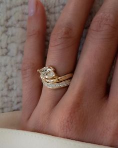 a woman's hand with a gold ring and diamond wedding band on top of it