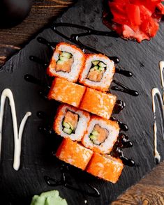 sushi on a slate board with sauce drizzled over it and garnished with cucumbers