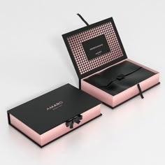 an open pink box with a black bow on the front and inside, sitting on a white surface