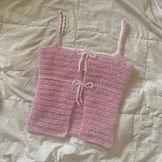 a pink crocheted top laying on a white bed with a knot at the bottom