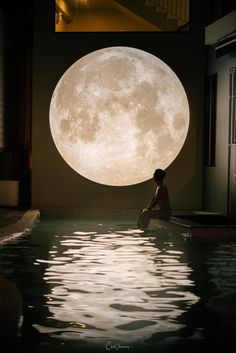 a person sitting in the middle of a pool with a large moon above them,