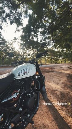 a motorcycle parked on the side of a dirt road next to some trees and grass