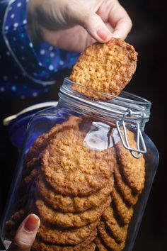 a person holding a jar full of cookies in their left hand and reaching for the cookie