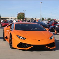 an orange sports car parked in a parking lot with people standing around and looking at it