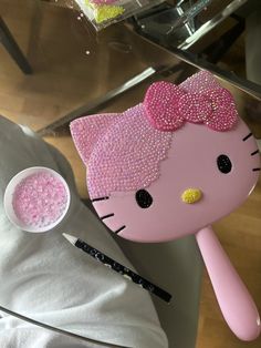 a pink hello kitty doll next to a bowl of glitter and a brush on a table