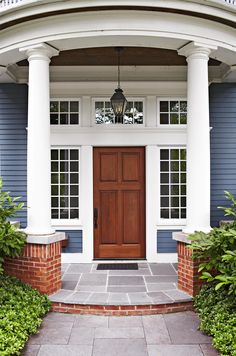 a blue house with white columns and a wooden door on the front porch, surrounded by greenery