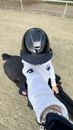 a small child wearing a helmet sitting on top of a person's leg in the dirt