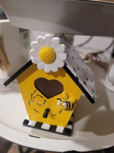 a yellow birdhouse with a flower on top of it's roof and eyes