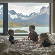 three children are sitting on a bed looking out the window at mountains and snow capped peaks