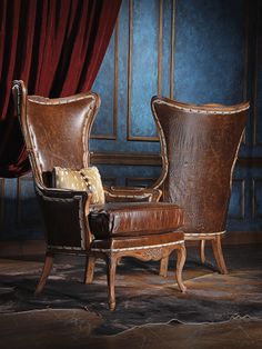 two brown leather chairs sitting next to each other in front of a red drapes