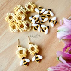 three pairs of bee earrings on a table next to pink flowers and purple lilies