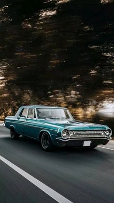 an old blue car driving down the road