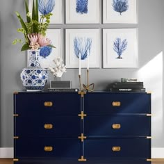 a blue and white dresser with four pictures on the wall above it, along with flowers