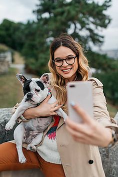 a woman taking a photo with her cell phone while holding a dog in her lap