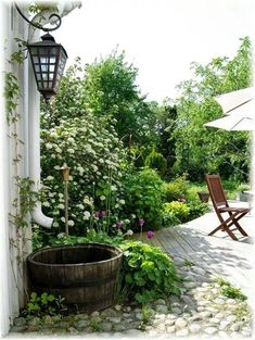 a wooden barrel sitting in the middle of a garden next to a chair and umbrella