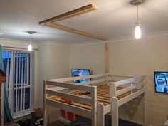 a man standing next to a bunk bed in a room with two monitors on the wall