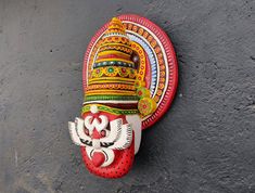 a red and yellow mask hanging on the side of a gray wall next to a black floor