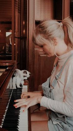 a woman is playing the piano with her cat on the other side and looking at it