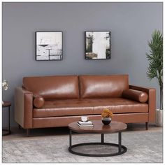 a brown leather couch sitting in a living room next to two pictures on the wall