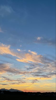 an airplane is flying high in the sky at sunset with clouds and mountains behind it