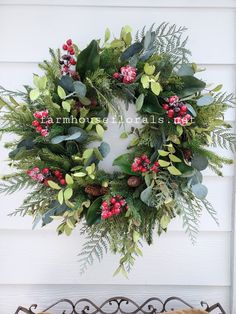 a christmas wreath hanging on the side of a white house with greenery and berries