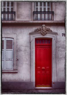 a red door is in front of an old building with shutters on the windows