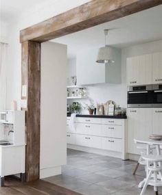 an open kitchen and dining room area with white cabinets, wood flooring and wooden beams